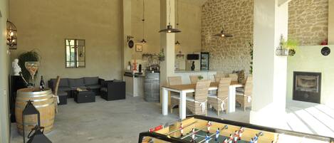 A spacious living area with a foosball table, comfortable seating, a kitchen area, and a stone wall.