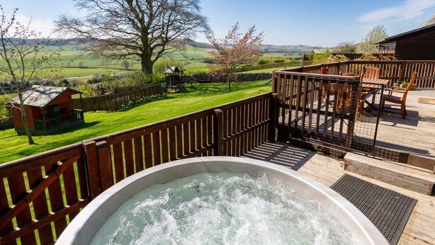 A hot tub on a wooden deck with a view of a green landscape and a small wooden structure in the background. - Douglas Fir Lodge With Hot Tub Near Cupar, Fife (Cupar)