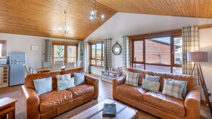 A cozy living room with two leather sofas, a coffee table, and a dining area with a table and chairs. - Douglas Fir Lodge With Hot Tub Near Cupar, Fife (Cupar)
