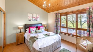 A bedroom with a wooden ceiling, a bed with multiple pillows, a nightstand with a lamp, and a window with curtains. - Douglas Fir Lodge With Hot Tub Near Cupar, Fife (Cupar)