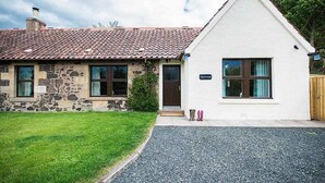 Une maison en pierre à deux étages, avec une façade blanche, un toit en tuiles et une allée gravillonnée.