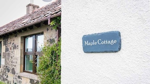 Une petite maison en pierre avec un toit d’ardoise et une enseigne indiquant « Maple Cottage ».