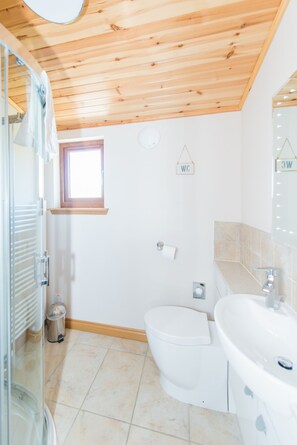 Un baño con techo de madera, inodoro, lavamanos y una pequeña ventana.