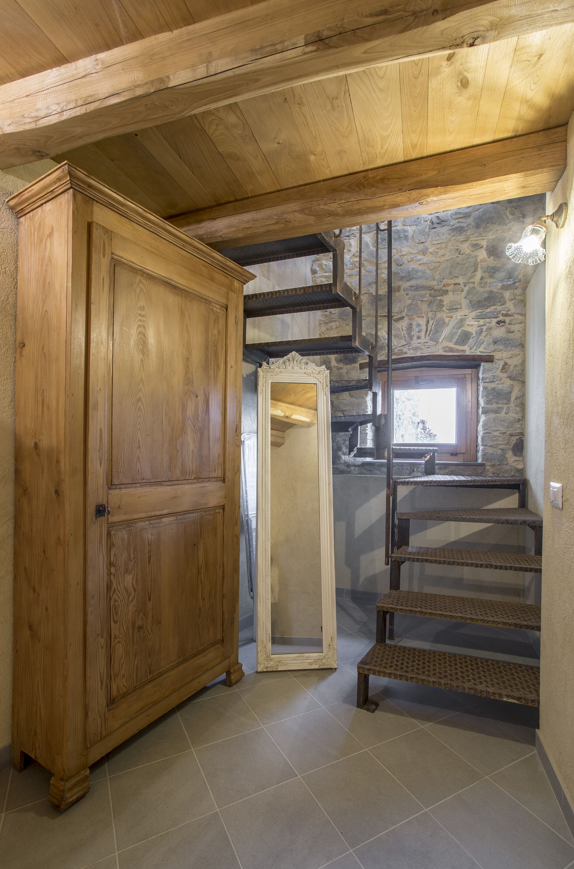 A wooden wardrobe, a mirror, and a staircase in a room with stone walls and wooden beams.
