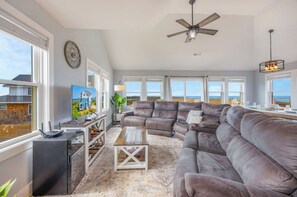 A spacious living room with a large sectional sofa, a ceiling fan, and a view of the ocean through large windows.