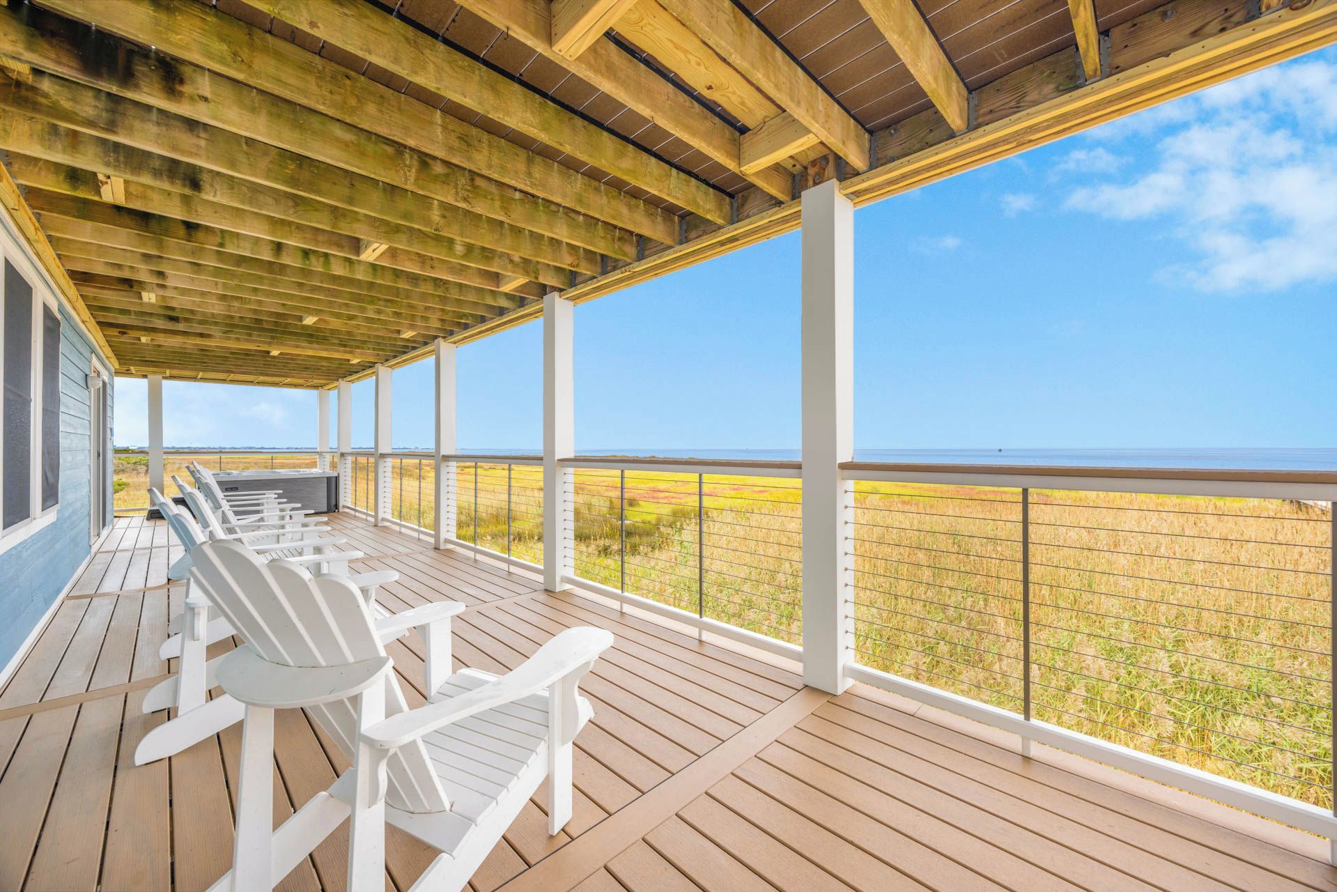Ein überdachter Außenbereich mit Holzterrasse, weißen Stühlen und Blick auf das Meer.