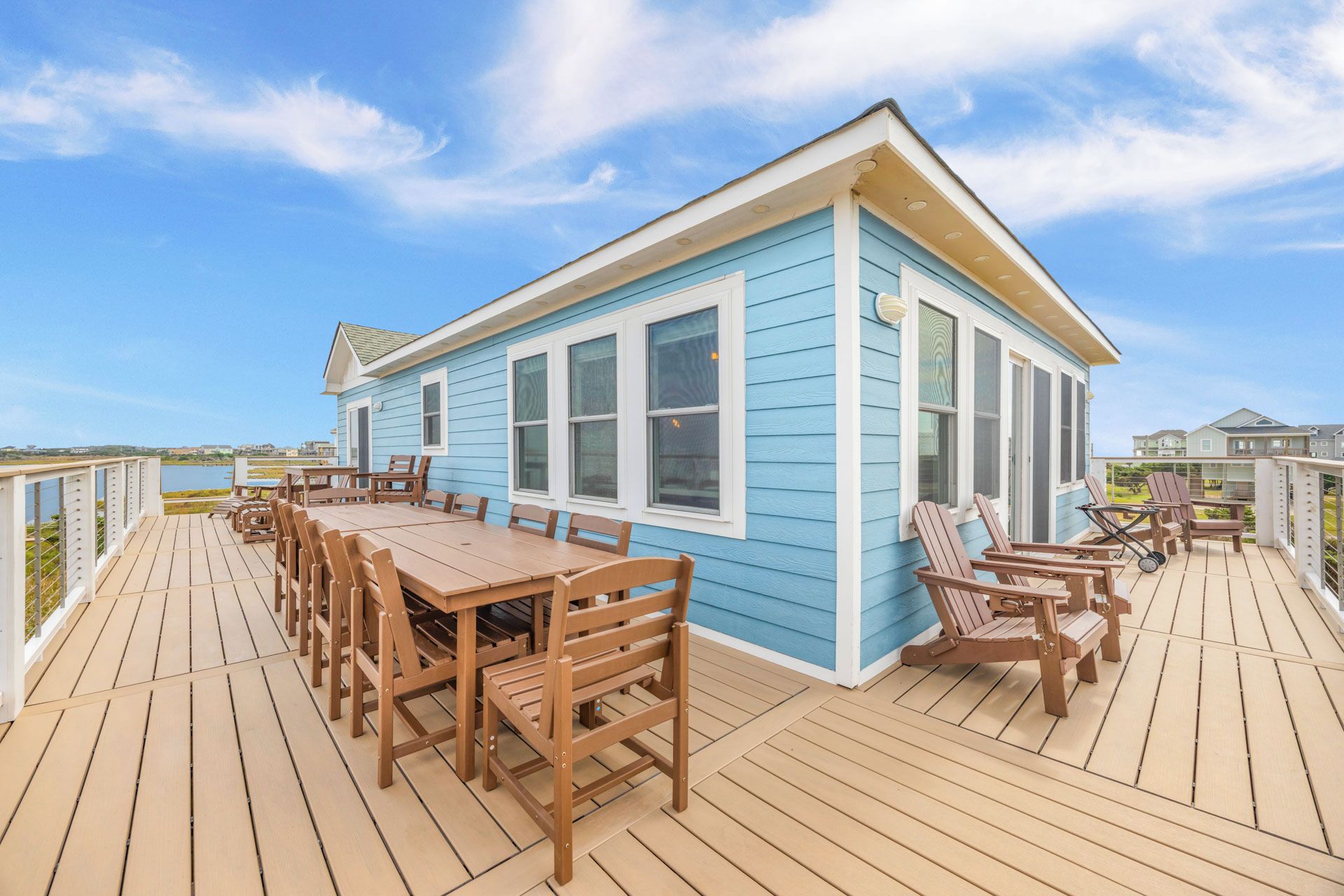 A blue house with a deck, wooden furniture, and a view of the water.