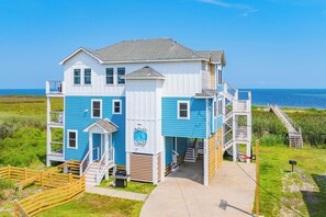 A multi-story building with a blue exterior, a visible staircase, and a view of the ocean. - Soundfront Dog Friendly Home with Hot Tub, Game Room, Easy Windsports Access (Frisco)
