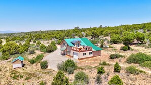 A two-story house with a green roof, surrounded by a dry, bushy landscape. - Stunning Canyon-Rim Retreat on the Dolores River in beautiful SW Colorado. (Dove Creek)
