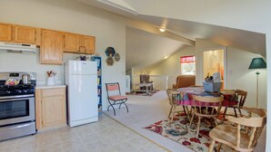 A spacious kitchen with wooden cabinets, a refrigerator, and a stove. There is a dining area with a table and chairs, and a living room with a sofa and a lamp. - Stunning Canyon-Rim Retreat on the Dolores River in beautiful SW Colorado. (Dove Creek)