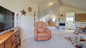 A spacious living room with a leather recliner, a flat-screen TV on a wooden cabinet, and a kitchen in the background. - Stunning Canyon-Rim Retreat on the Dolores River in beautiful SW Colorado. (Dove Creek)