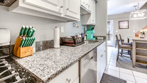 Una cocina con gabinetes blancos, encimeras de granito y un comedor con mesa y sillas.