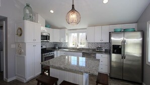 Une cuisine moderne avec des meubles blancs, des comptoirs en granit, un réfrigérateur en acier inoxydable et un luminaire suspendu.