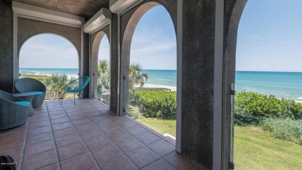 A covered patio with a view of the ocean, featuring a seating area with chairs and a tiled floor. - Beach front Condo with amazing water views! (Indialantic)