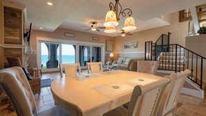 A spacious dining area with a large table, comfortable chairs, and a view of the ocean through large windows. - Beach front Condo with amazing water views! (Indialantic)