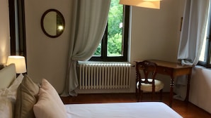 Un dormitori amb llit, escriptori, cadira, radiador, finestra amb cortines i mirall a la paret.
