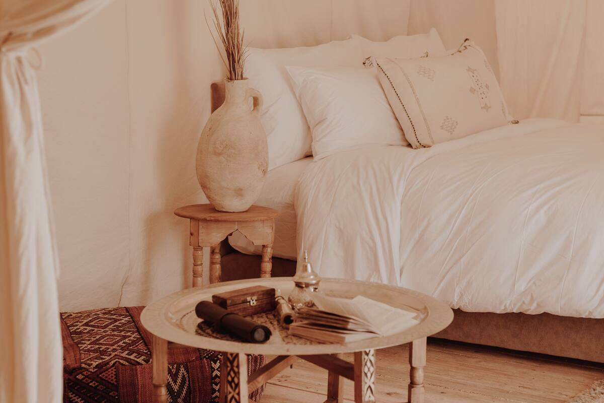 Ein Schlafzimmer mit einem Bett, einem Nachttisch mit einer Vase und einem kleinen Tisch mit zusammengerollten Gegenständen.