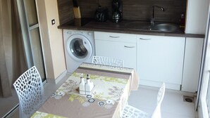 A compact kitchen with a microwave, coffee maker, and sink. There is a washing machine and a dining table with chairs. - Comfortable studio apartment in Le Gosier (Le Gosier)
