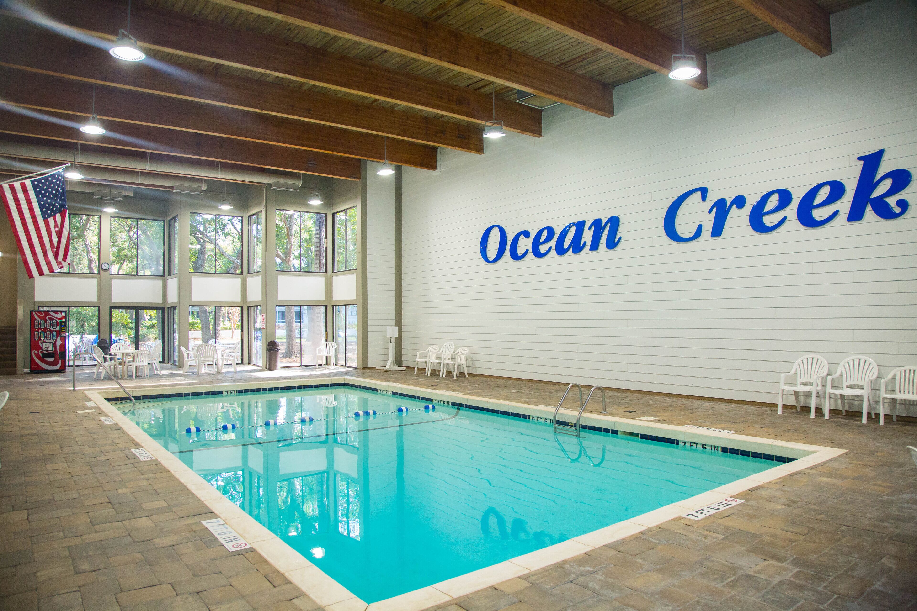 An indoor swimming pool with a view of trees outside, a Coca-Cola vending machine, and a sign reading 'Ocean Creek'.