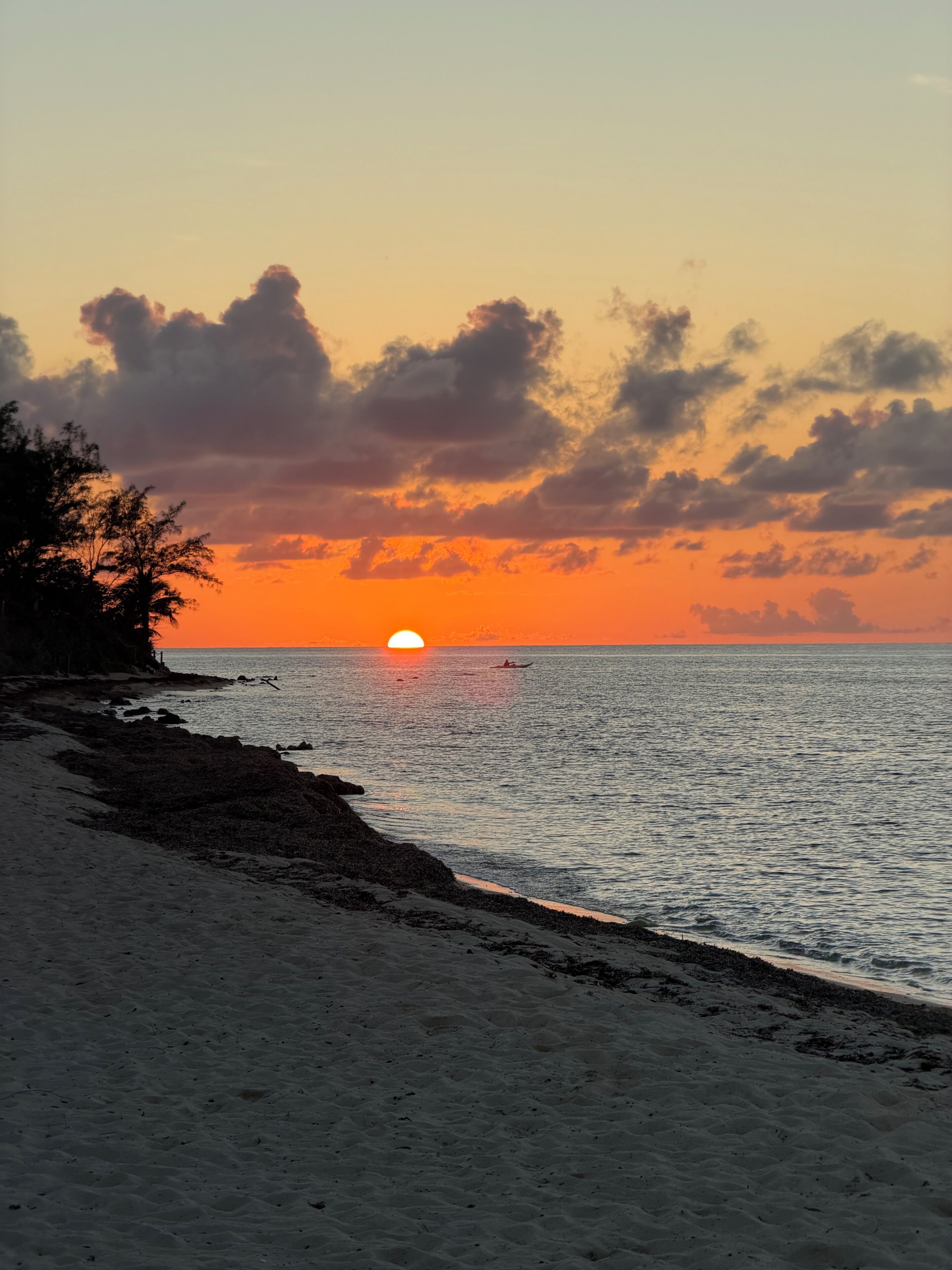 A beach with a sunset, calm sea, and a boat in the distance.