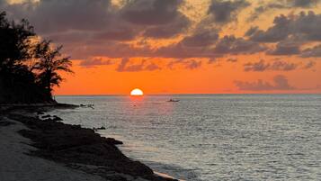 A beach with a sunset, calm sea, and a boat in the distance.