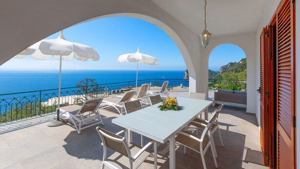 A terrace with white furniture, white umbrellas, and a view of the sea.