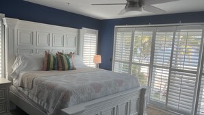 A bedroom with a large bed, white headboard, and a ceiling fan. - Steps away from the sugar white sands and blue water!! (Fort Myers Beach)