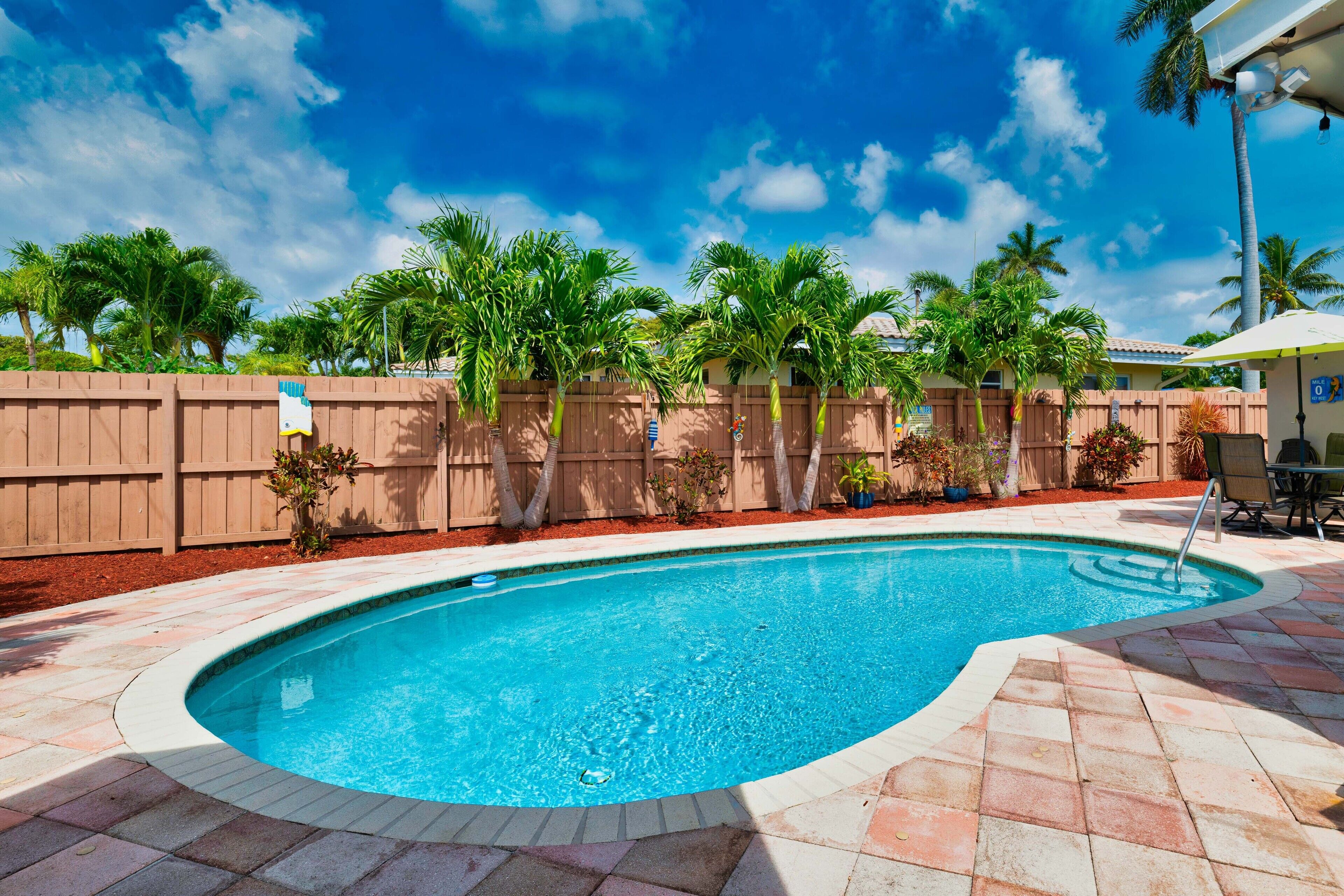 A swimming pool with a curved edge, surrounded by a wooden fence and palm trees.