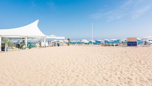 Ein Strand mit einer weißen Zelthalle, Sonnenschirmen und einem Schild mit der Aufschrift 'blue bar'.