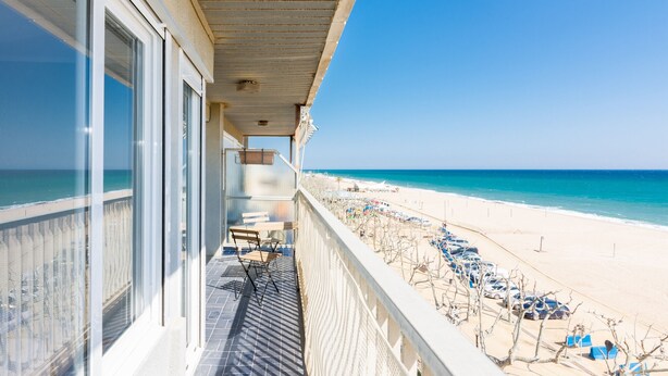 Ein Balkon mit Blick auf einen Strand, eine Reihe geparkter Autos und einen klaren, blauen Himmel.