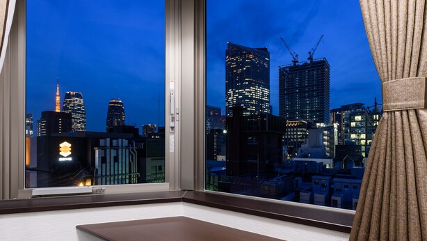 A corner room with a desk, chair, and a view of a cityscape at dusk. - Shimbashi Urban Hotel (Tokyo)
