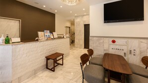 A hotel reception area with a marble counter, wooden chairs, a table, a chandelier, and a flat-screen TV mounted on the wall. - Shimbashi Urban Hotel (Tokyo)