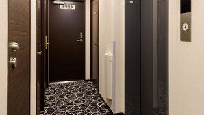 A hotel hallway with a patterned floor, a door with a sign, and an elevator. - Shimbashi Urban Hotel (Tokyo)