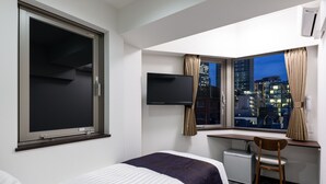 A hotel room with a bed, a desk, a chair, a TV, and a window with a city view. - Shimbashi Urban Hotel (Tokyo)