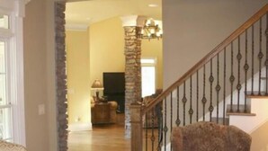 A spacious living room with a high ceiling, a stone pillar, and a staircase with a wooden railing. - Beautiful -Spacious Home @ Lake Lanier (Flowery Branch)
