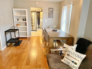 A modern kitchen with a built-in refrigerator, a dining area with a wooden table and chairs, and a cozy seating area with a couch and a welcome pillow.