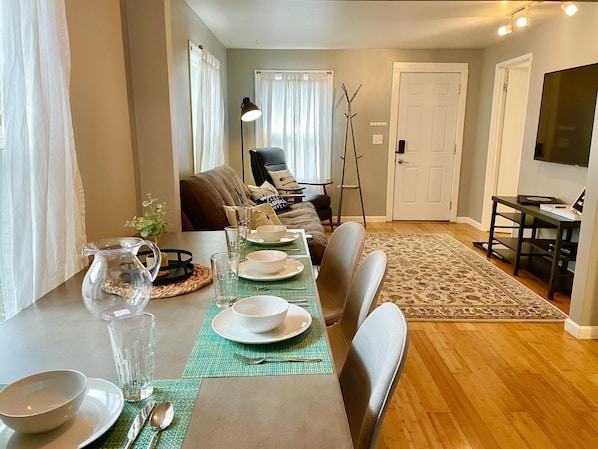 A dining area with a table set for four, a sofa, a TV, and a door in the background.