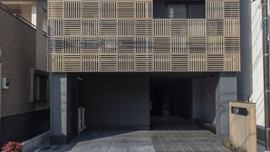 Un edificio moderno con fachada geométrica, entrada cubierta y área delimitada por una verja.
