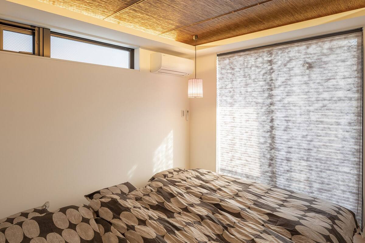 A room with a sloped ceiling, a large window with blinds, and a patterned bedspread.