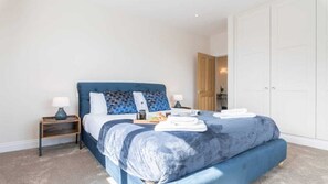 A bedroom with a large bed, two bedside tables, a wardrobe, and a bathroom visible through an open door. - South Quay Penthouse - 2 Bedroom - Parking - River (Great Yarmouth)
