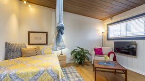 Een slaapkamer met een bed, nachtkastje, lamp en een groot raam met zonwering.