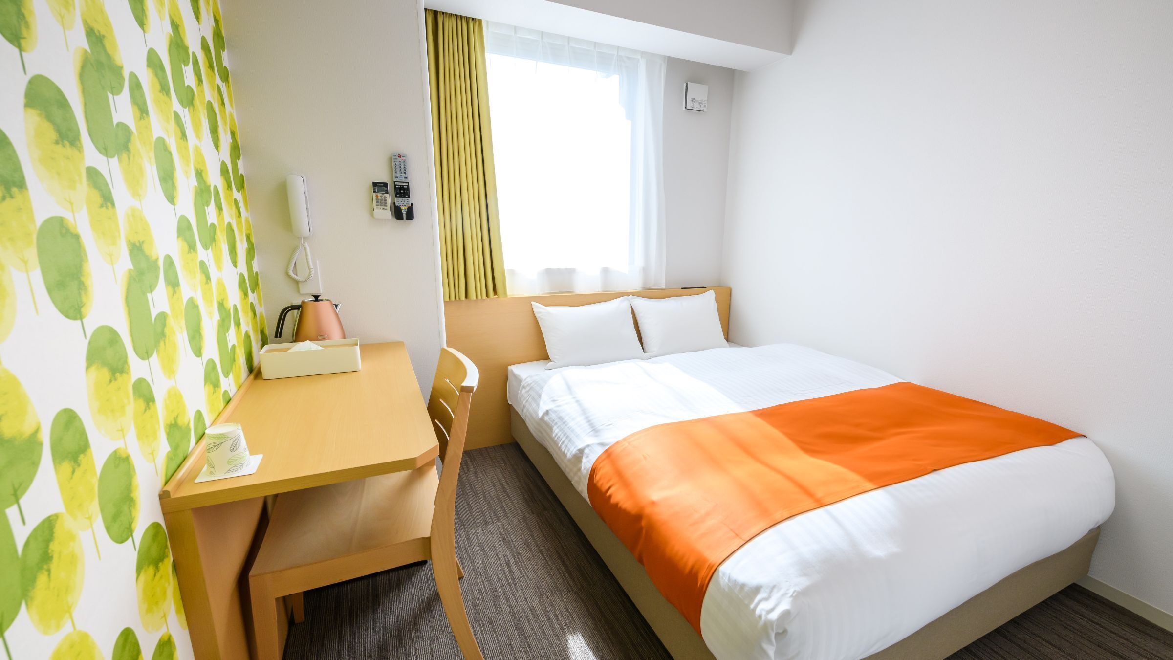 Une chambre d’hôtel équipée d’un lit, d’un bureau, d’une chaise, d’un téléphone et d’une fenêtre avec des rideaux.