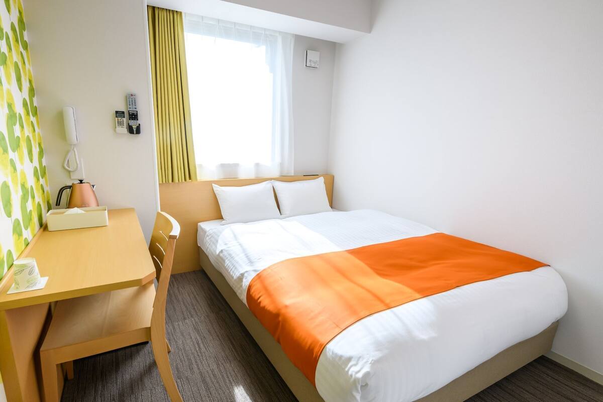 Ein Hotelzimmer mit Bett, Schreibtisch, Stuhl, Telefon und einem fenster mit Vorhängen.