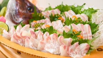 A wooden tray with sliced fish, garnished with green leaves and orange slices.