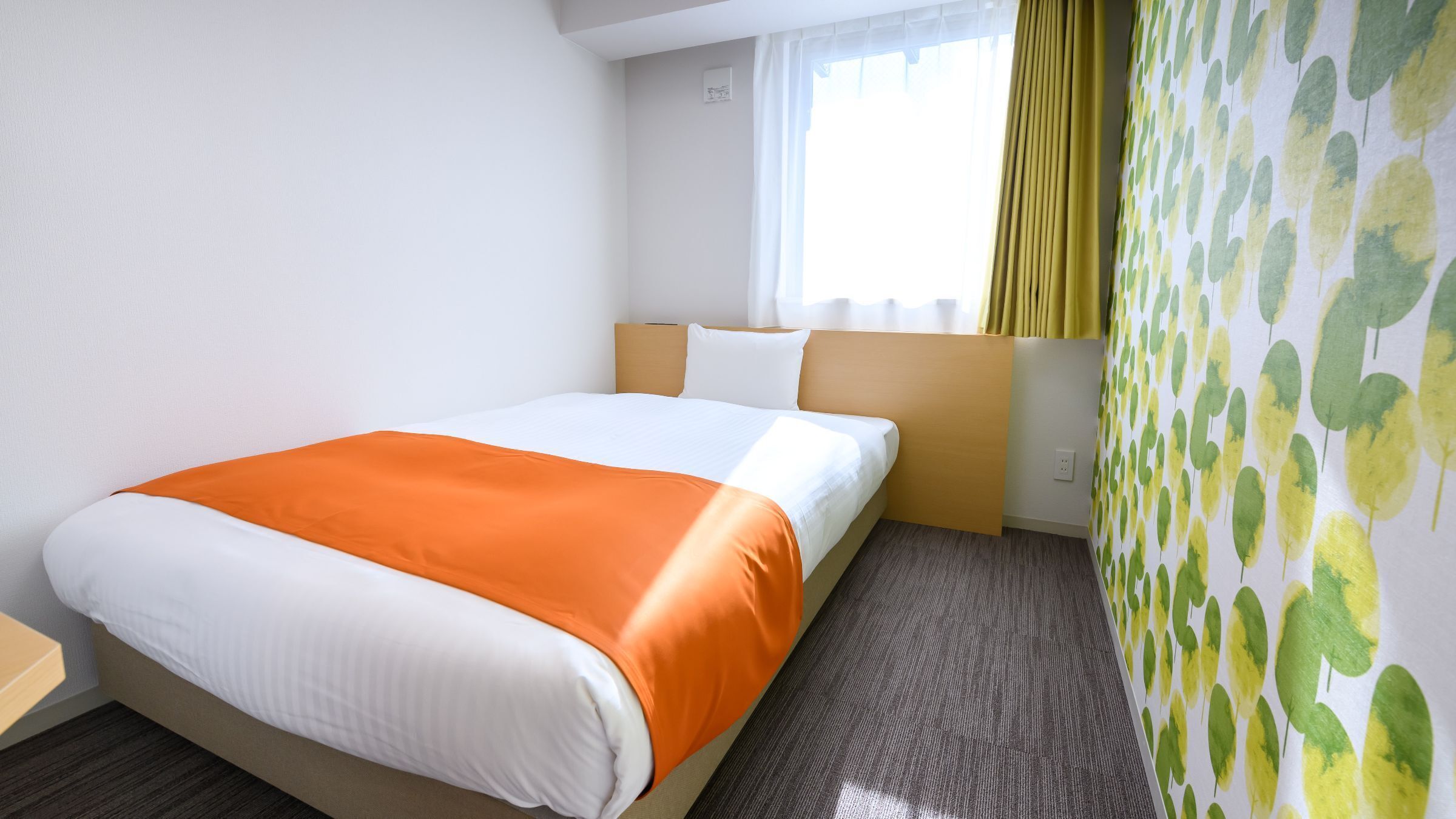 Une chambre d’hôtel avec un lit, une fenêtre avec des rideaux et un mur orné d’un motif de feuilles.