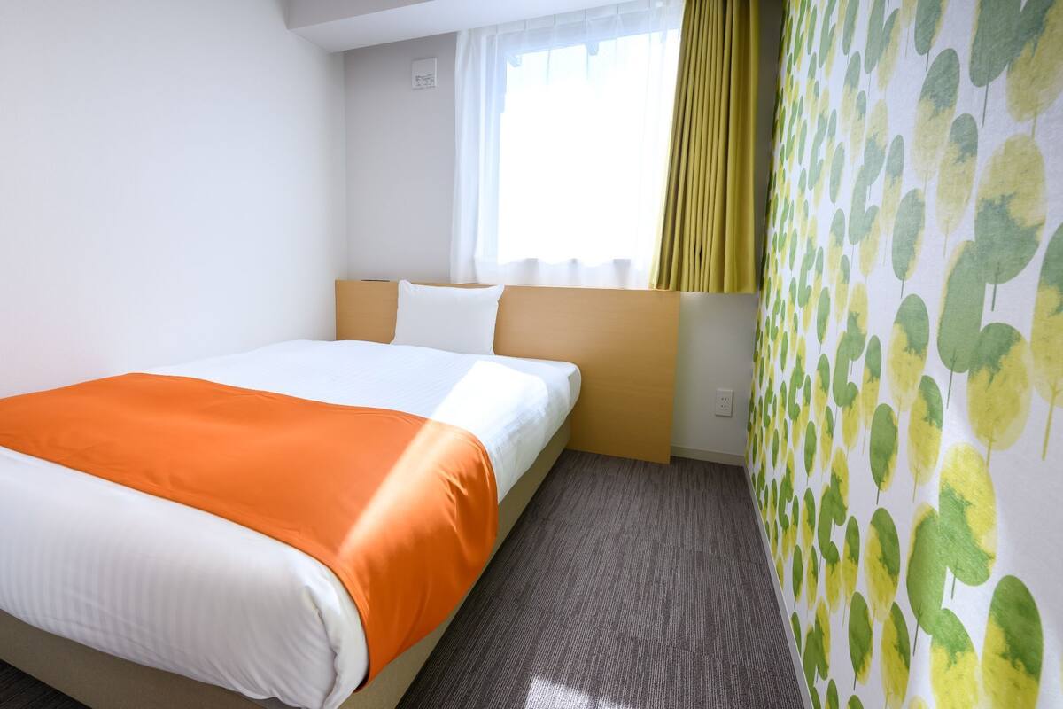 Ein Hotelzimmer mit einem Bett, einem Fenster mit Vorhängen und einer Wand mit einem Blattmuster.