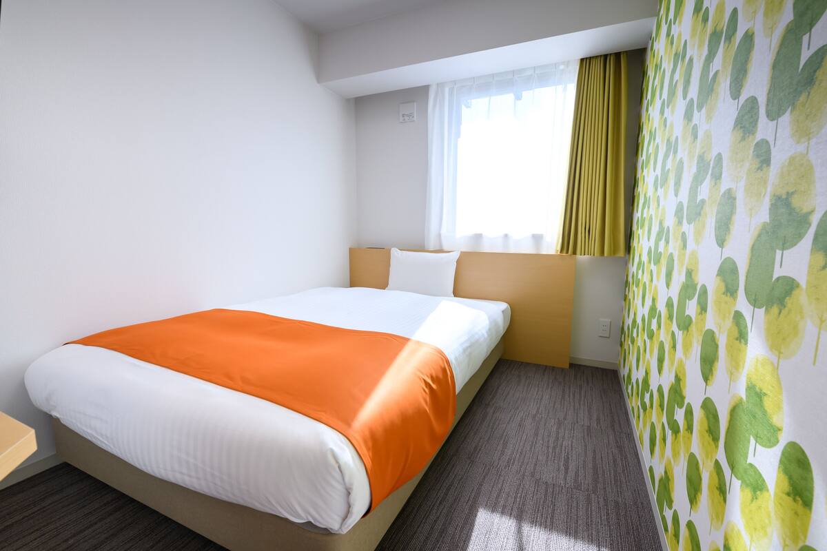 Ein Hotelzimmer mit einem Bett, einem Fenster mit Vorhängen und einer Wand mit einem Blattmuster.