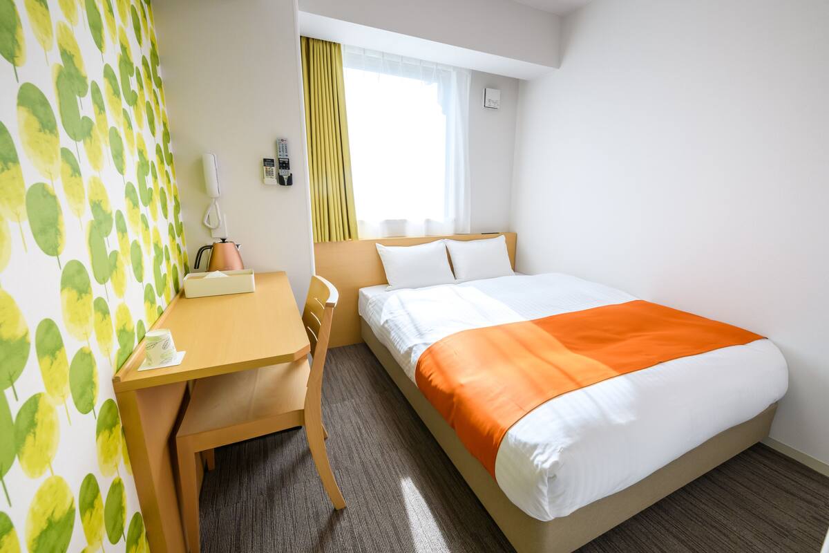 Ein Hotelzimmer mit einem Bett, einem Schreibtisch, einem Stuhl, einem Telefon und einem Vorhangfenster.