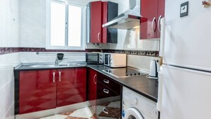 A compact kitchen with red cabinets, a microwave, a toaster, and a washing machine. - Apartamento La Perla flamenca (Cádiz)