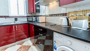 A compact kitchen with red cabinets, a built-in oven, a microwave, a toaster, and a washing machine. - Apartamento La Perla flamenca (Cádiz)